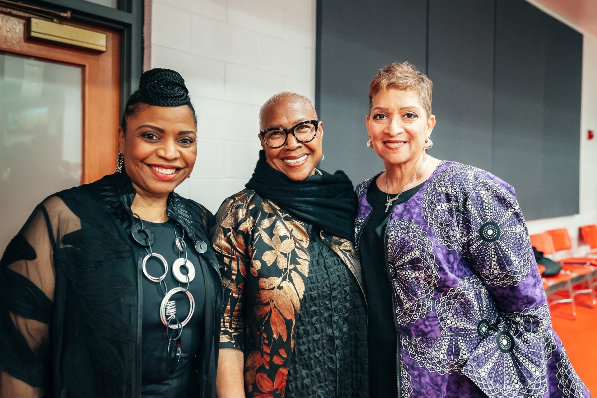 Three woman standing next to eachother, posing for the camera, all the woman have big smiles on their faces.